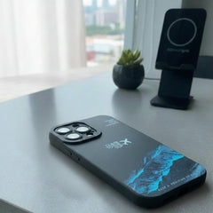 Black smartphone with a blue screen on a desk next to a plant and phone stand.