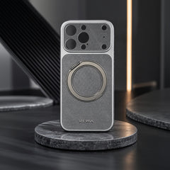 A silver textured phone case with a circular magnetic ring and camera cutouts, displayed on a round marble stand against a dark background.
