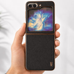 A hand holding a black leather flip phone case with a gold-tone metal frame and a colorful display showing a blue and purple flower design.