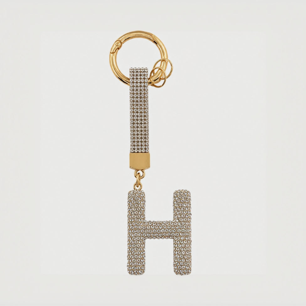 A gold-tone keychain featuring a large letter 'H' charm and a matching key ring, both heavily embellished with clear rhinestones, set against a plain white background.