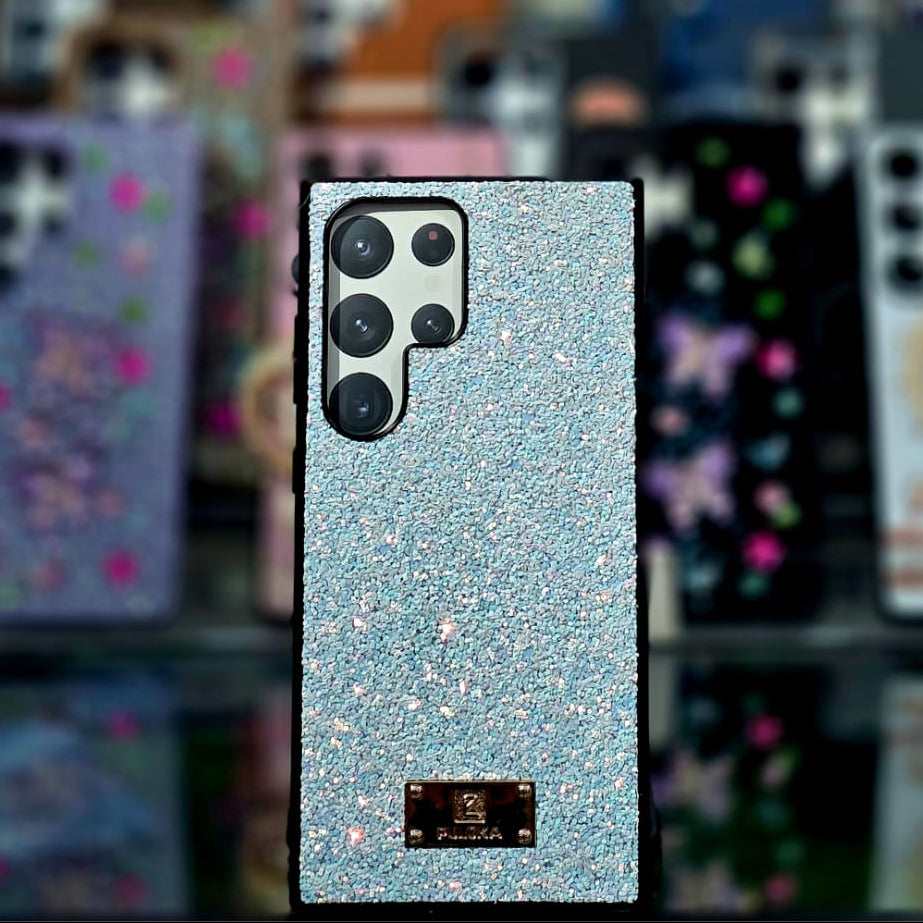 Glittery phone case with brand logo against a blurred background of other phone cases.