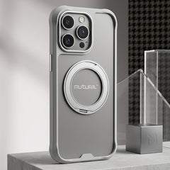 A silver Mutual phone case with an integrated circular magnetic ring stand, shown standing upright on a concrete pedestal in a modern studio setting.