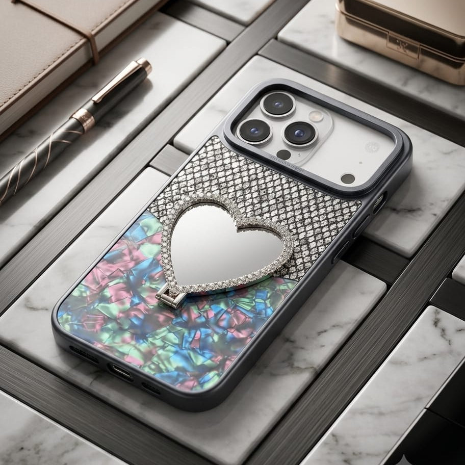 A luxury phone case featuring a silver rhinestone-embellished heart pendant, a colorful iridescent butterfly wing design, and a textured silver mesh back, displayed on a marble surface with a luxury watch and notebook nearby.