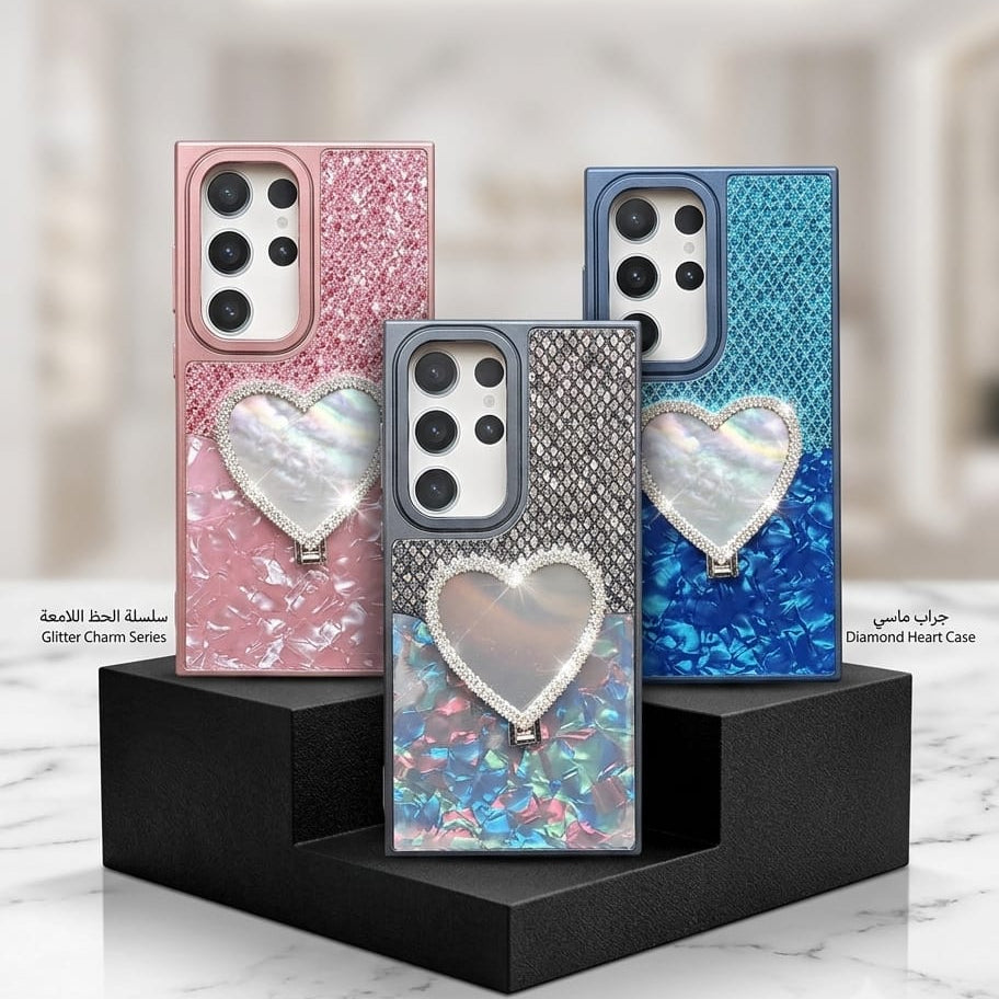 Three smartphone cases displayed on black stands in a clean indoor setting. The center case is shown in front, with a glittery iridescent heart charm and a blue patterned back.