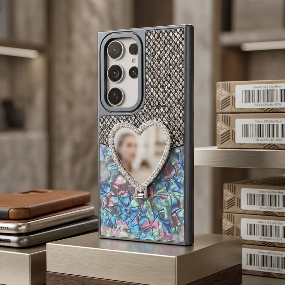 A luxury smartphone case displayed on a wooden and metallic stand in a boutique setting. The case features a textured silver mesh top section, a central heart-shaped crystal frame containing a blurred photo, and a colorful blue, pink, and green floral mosaic bottom section.