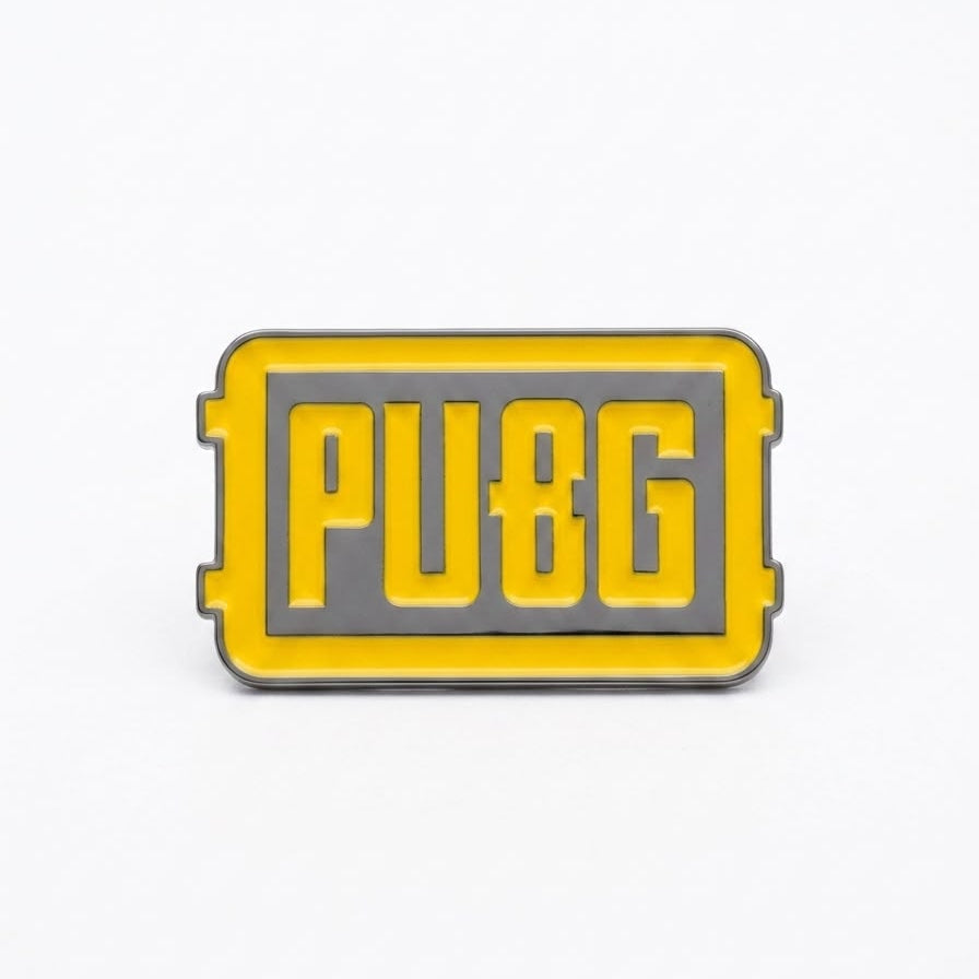 A rectangular yellow and gray enamel pin featuring the text 'PUBG' in bold yellow letters on a gray background, set against a plain white studio backdrop.