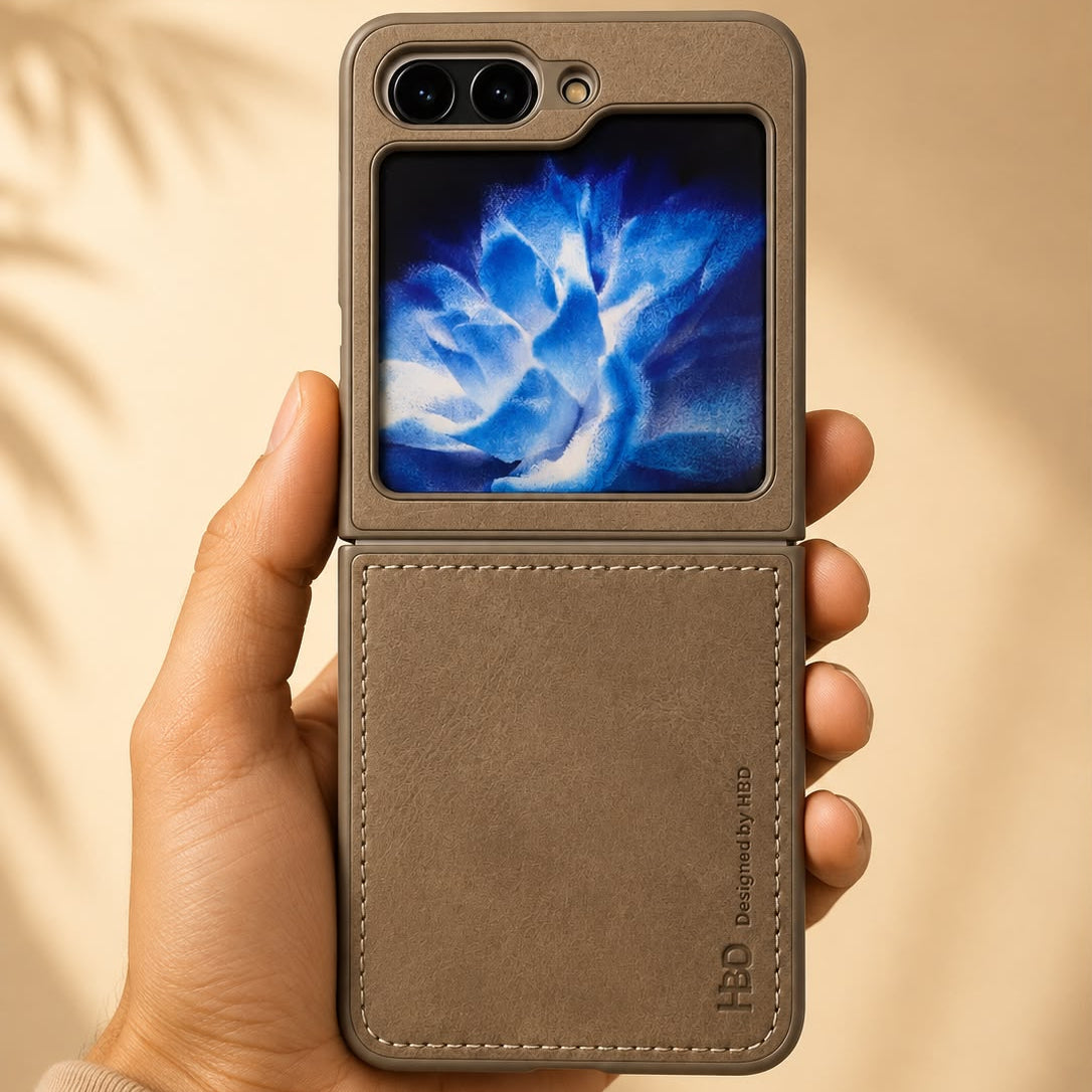 A hand holding a brown leather flip phone case with a built-in display screen showing a blue flower wallpaper. The case has a textured leather back, a stitched edge, and a debossed logo on the bottom right.