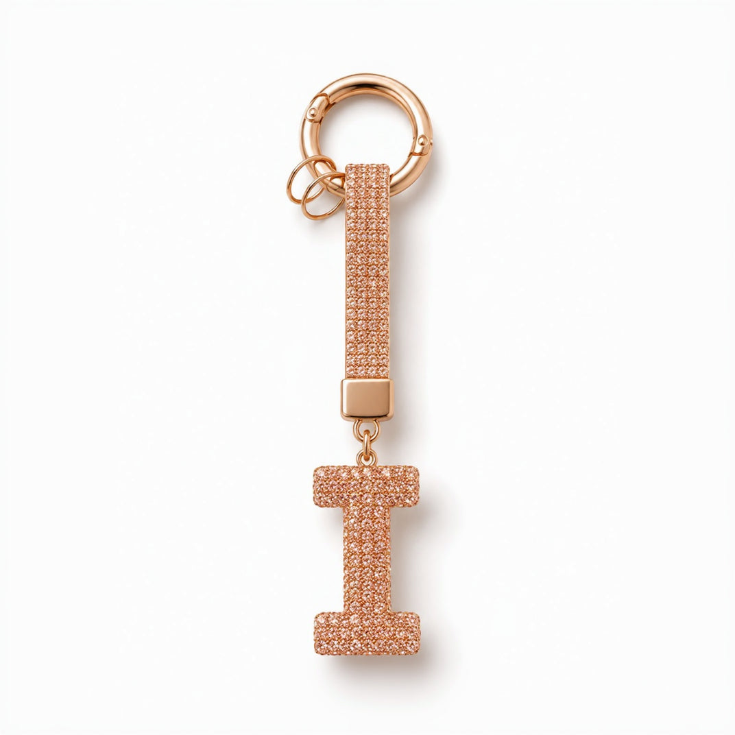 A rose gold initial keychain featuring a large letter 'I' charm paved with clear rhinestones, attached to a matching rhinestone-embellished strap and a split key ring, shown on a white background.
